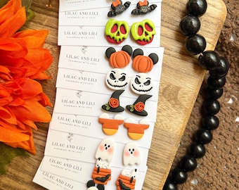 Könnte beinhalten: Eine Sammlung von Ohrsteckern zum Thema Halloween. Zu den Designs gehören Geister, Kürbislaternen, Hexenhüte, Kürbisse und Zuckermais. Die Ohrringe werden auf Karten mit dem Text "LILAC AND LILI HANDMADE WITH LOVE" präsentiert.