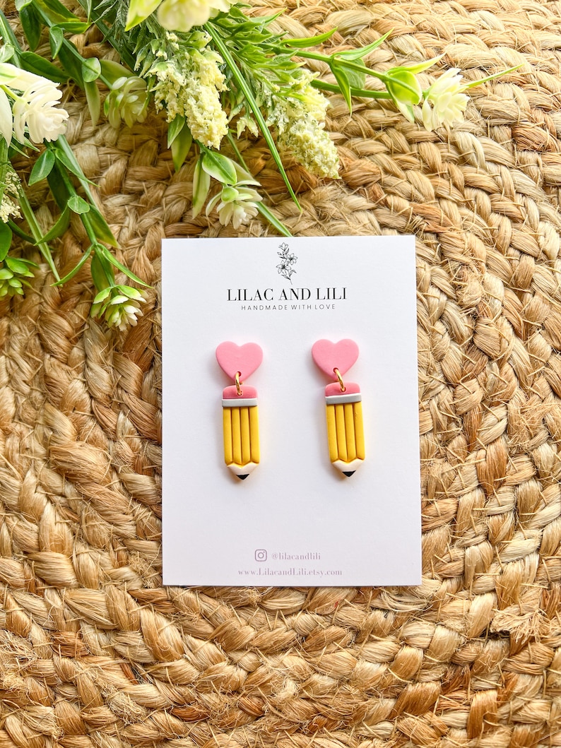 Pu&ograve; includere: Un paio di orecchini a forma di cuore rosa e matita gialla. Gli orecchini sono fatti a mano con amore da Lilac and Lili. Gli orecchini sono disponibili per l'acquisto su Etsy.