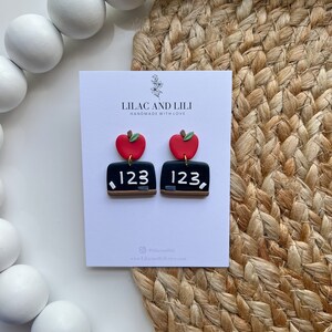 May include: A pair of red apple and chalkboard earrings with the number 123 on each chalkboard. The earrings are handmade by Lilac and Lili.