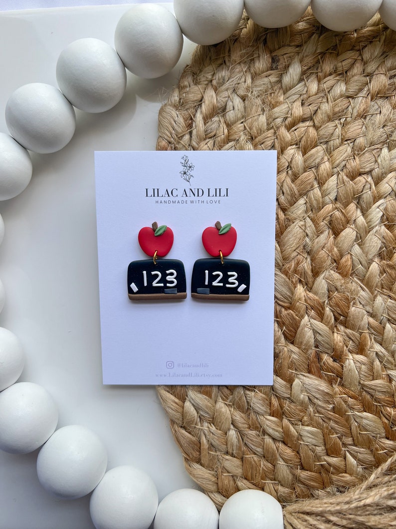 May include: A pair of red apple and chalkboard earrings with the number 123 on each chalkboard. The earrings are handmade by Lilac and Lili.