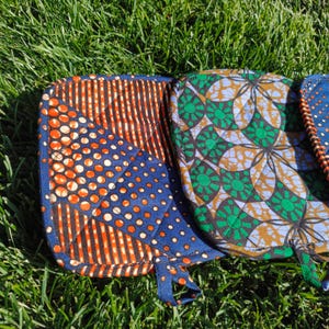 May include: Close-up of colorful quilted oven mitts with various patterns. One mitt features a blue background with orange circles and stripes. Another has a green and brown floral design. Each mitt has a loop for hanging.