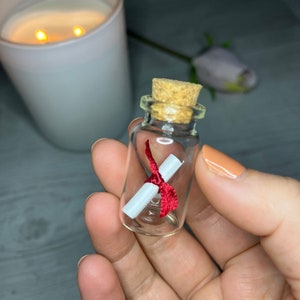 May include: A small glass bottle with a cork stopper, containing a rolled up piece of paper tied with a red ribbon.
