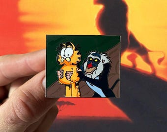 May include: A cartoon pin featuring Garfield the cat being held by Scar from The Lion King. Garfield is orange and white, and Scar is black and white with a red nose. The pin is set against a green background.