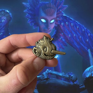 Puede incluir: Un pin de color dorado que presenta una criatura de madera de estilo de dibujos animados con una nariz grande y una expresión caprichosa. La criatura se encuentra sobre un fondo azul y morado con una criatura de madera más grande y detallada en el fondo.