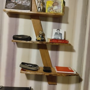 May include: A wooden shelf unit with three shelves. The top shelf has a photo, a figurine of a knight, and a box with a mushroom design. The middle shelf has a small bag, a figurine, a book, and a book titled "LAINE". The bottom shelf has a bag, a wallet, and a red book titled "BOICE".