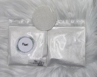 May include: Two clear plastic bags filled with white glitter, labeled "Pearl". The bags are on a white fluffy surface. The text "The Wright Glitter" is visible on the bottom of the image.