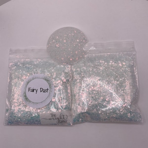 May include: Two clear plastic bags filled with iridescent light blue and white glitter. The bags are labeled "Fairy Dust" and "The Wright Glitter".