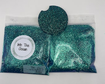 以下が含まれることがあります： 「Into The Ocean」と「The Wright Glitter」の文字が書かれた、2つのターコイズグリーンのグリッターが入った袋。ターコイズグリーンのグリッター製のコースターも写っています。