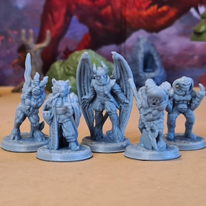 Op de afbeelding: Een verzameling van vijf grijze fantasie miniaturen, elk met unieke ontwerpen. De figuren omvatten een gevleugelde demon, een gehoornd wezen en andere monsterachtige personages. Ze staan op ronde bases.