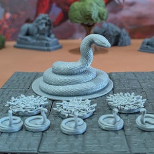 Peut inclure: Ensemble de figurines grises pour jeu de rôle fantastique. L'ensemble comprend un serpent enroulé, de petites figurines de serpent et des éléments de terrain circulaires. Les pièces sont conçues pour les jeux de table et sont en matériau gris clair.