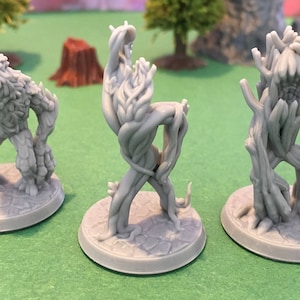 Puede incluir: Tres figuras en miniatura de plástico gris de criaturas arbóreas. Las figuras están de pie sobre bases redondas. Las figuras son todas diferentes, una tiene una forma más humanoide, otra es más como una vid retorcida y otra es más como un tronco de árbol.