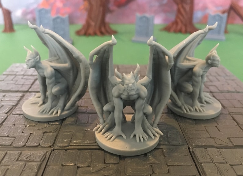 Puede incluir: Tres figuras de g&aacute;rgola grises con alas, cada una sentada sobre una base cuadrada gris. Las g&aacute;rgolas tienen dientes y garras afiladas.