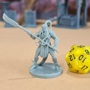 Puede incluir: Una figura en miniatura gris de una criatura humanoide con una lanza y una espada, de pie sobre una base circular. Un dado amarillo de múltiples caras está al lado de la figura. La miniatura es probablemente para juegos de mesa.