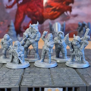 May include: A collection of gray miniature fantasy figures, including a minotaur, a figure with a rifle, and a figure in an astronaut suit. The figures are arranged on a gray, textured surface, with a blurred background.