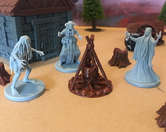 May include: A miniature tabletop gaming set with a brown cauldron over a fire, a gray stone building, and three gray figures. The figures are a woman with horns, a ghost-like figure, and a creature with long hair.