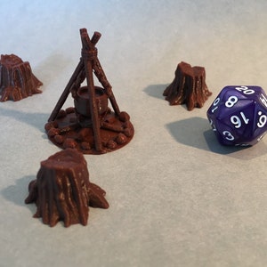 May include: A purple 20-sided die with white numbers sits on a table next to a brown 3D printed miniature of a campfire with a cauldron and three tree stumps.
