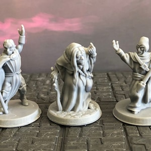 Puede incluir: Tres figuras en miniatura pintadas de gris de magos, cada una con una pose diferente y sosteniendo un bastón. Las figuras están de pie sobre bases redondas.