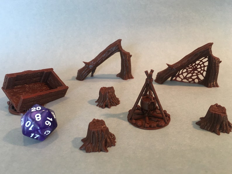 May include: A set of brown 3D printed miniature forest scenery pieces, including a fallen log, a log with a web, a campfire, and four tree stumps. A purple 20-sided die is also included.