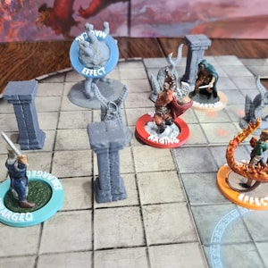 May include: A tabletop role-playing game setup with miniature figures and game pieces. The figures are on colored bases with text like "Raging" and "Effect". Gray pillars and a game board are also visible.