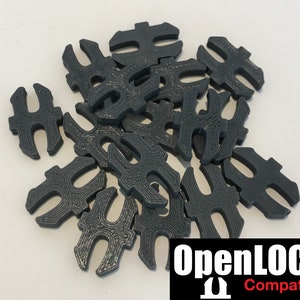 以下が含まれることがあります： ユニークなインターロックデザインの濃いグレーのプラスチック製の部品の山。部品には「OpenLOCK Compatible」とラベル付けされています。