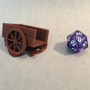 May include: A brown wooden miniature wagon with a single wheel. The wagon is sitting on a white surface next to a purple 20-sided die with white numbers.