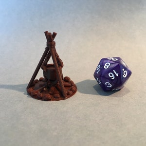 May include: A brown 3D printed miniature of a campfire with a cauldron hanging over the flames. A purple 20-sided die with white numbers is in the background.