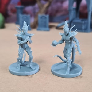 Op de afbeelding: Twee grijze miniatuur fantasy figuren. Eén figuur houdt een bal vast, de andere heeft de armen gekruist. Beide hebben stekelige hoofd- en lichaamsontwerpen en staan op ronde bases. Achtergrond bevat miniatuurstructuren.