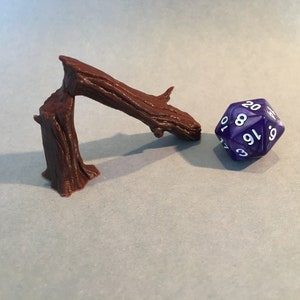 May include: A brown wooden tree branch with a textured surface, bent into a curved shape, and a purple 20-sided die with white numbers.