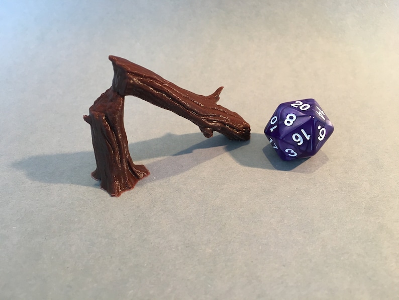 May include: A brown wooden tree branch with a textured surface, bent into a curved shape, and a purple 20-sided die with white numbers.