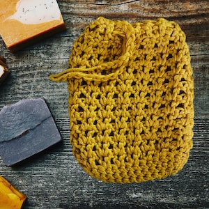 May include: A mustard yellow crocheted soap sack with a drawstring closure. The sack is made of a soft, textured yarn and is perfect for holding a bar of soap.
