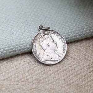 May include: A circular silver pendant featuring a profile of a crowned man, with the inscription "EDWARD VII KING & EMPEROR". The pendant has a small loop at the top for attaching to a chain or necklace.