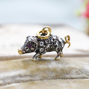 Puede incluir: Un amuleto de plata y oro en forma de cerdo, con un ojo de rubí y cubierto de pequeños diamantes.