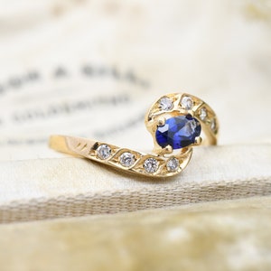 May include: A gold ring with a blue oval gemstone surrounded by smaller clear gemstones. The ring has a twisted band.