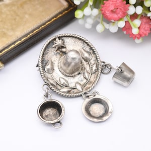 May include: A silver charm bracelet featuring a sombrero charm with three dangling charms: a small bucket, a small bowl, and a larger bowl.
