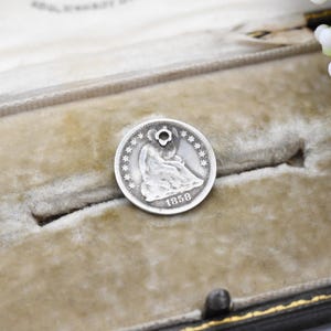 May include: A silver half dollar coin from 1858 with a hole drilled through the top. The coin is in a velvet-lined box.