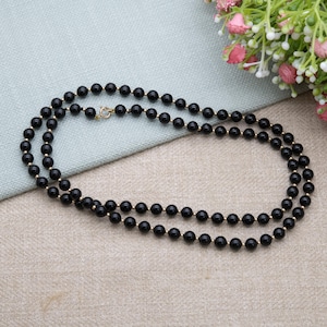 May include: A double-strand necklace featuring small, round, black beads interspersed with gold-colored beads. The necklace is secured with a gold-colored clasp and lies on a neutral-toned surface.