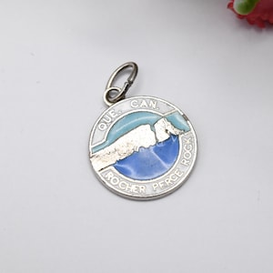 May include: Silver charm with blue and white enamel depicting a map of the Canadian province of Quebec, with the text "QUE. CAN. ROCHER PERCE ROCK" around the edge.