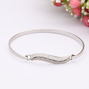 May include: A silver bangle bracelet with a wave-shaped design and small clear stones.