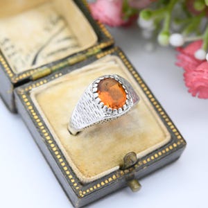 May include: A silver ring with a textured band and a large orange gemstone set in a silver bezel.