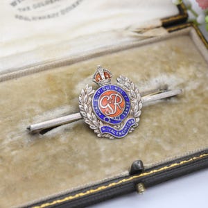 May include: A vintage Royal Engineers tie pin. The silver tie pin features a circular emblem with a crown, laurel wreath, and the text "Royal Engineers". The emblem has blue, orange, and silver details, and the text "HONI SOIT QUI MAL Y PENSE".