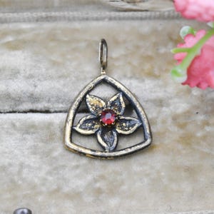May include: A vintage-style pendant featuring a flower design with a red gemstone center. The pendant is set within a triangular frame with gold and silver tones, creating a striking contrast. The floral element adds a touch of elegance.