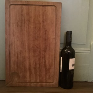 Könnte beinhalten: Ein großes, rechteckiges Schneidebrett aus Holz mit leicht abgerundeter Kante. Das Brett ist aus hellbraunem Holz und hat eine natürliche Oberfläche. Eine Flasche Rotwein steht neben dem Brett.