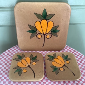 Könnte beinhalten: Set aus drei Keramik-Servierplatten mit braunem Hintergrund und einem stilisierten Blumendesign in Gelb, Grün und Orange.
