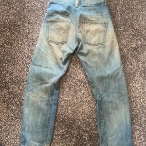 May include: Light blue denim jeans with a faded wash and two back pockets. The jeans have a red Levi's tag on the back pocket. The jeans are laid flat on a textured surface.