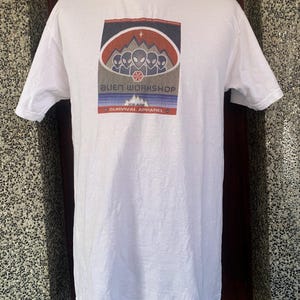 May include: White t-shirt with a graphic featuring the text "Alien Workshop" and the words "Survival Apparel." The graphic includes a mountain range, a star, and several alien figures in a rectangular design.