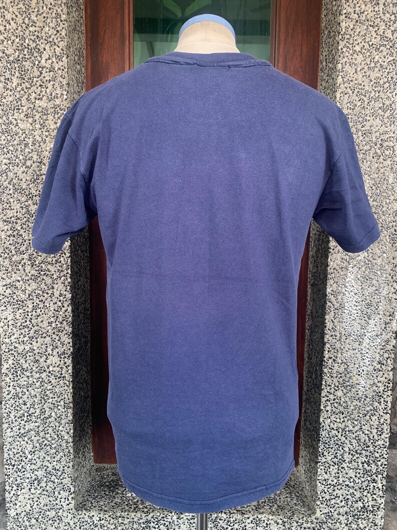 May include: A solid navy blue short-sleeved t-shirt. The shirt is made of a soft, slightly textured fabric. The neckline and sleeves have a worn appearance.