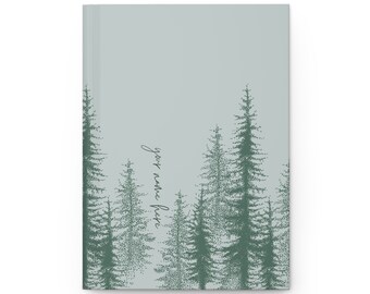 May include: A hardcover journal with a light blue cover featuring a forest design in shades of green. The design includes stylized evergreen trees and the text "your name here" in a script font.
