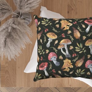 May include: A black throw pillow with a white border features a repeating pattern of watercolor mushrooms, leaves, and acorns on a dark green background.
