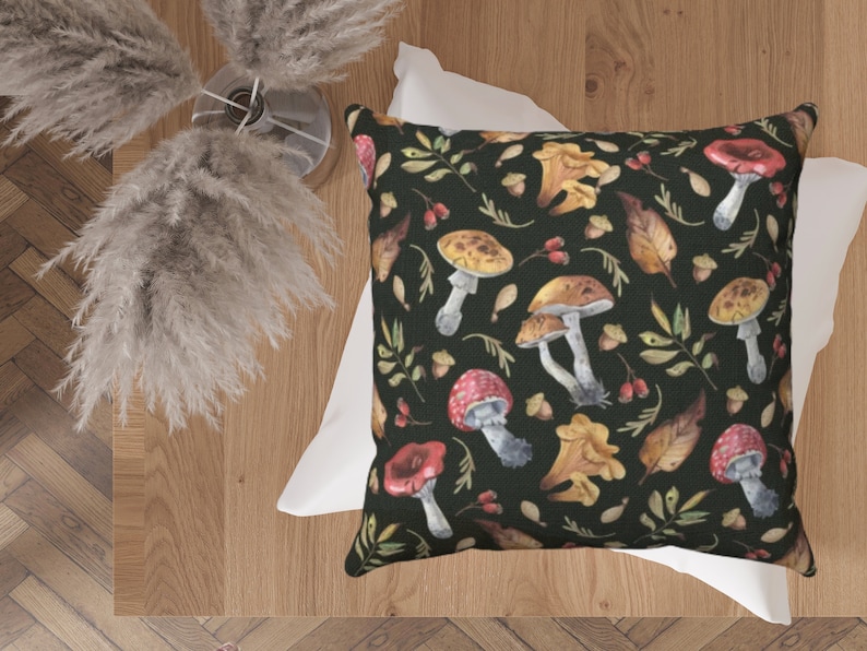 May include: A black throw pillow with a white border features a repeating pattern of watercolor mushrooms, leaves, and acorns on a dark green background.