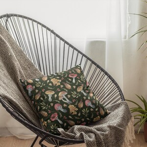 May include: A black metal chair with a brown and white throw blanket and a green pillow with a mushroom and leaf pattern.